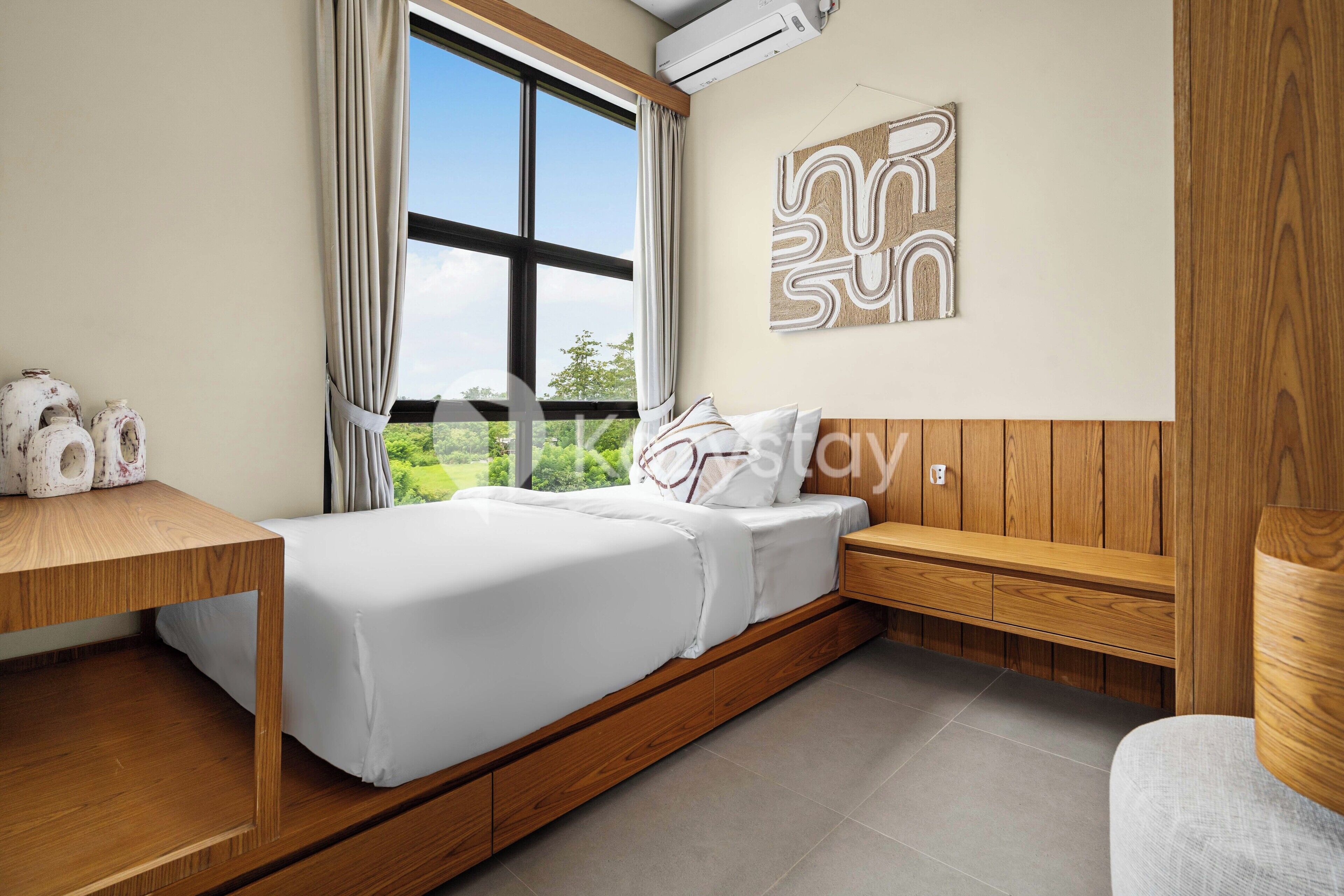 A modern bedroom with a wooden bed, a desk, and a view of greenery outside.