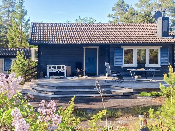 A house with a tiled roof, a porch with a table and chairs, and a small garden with flowers. - 5 Person Holiday Home in Graddo (Gräddö)