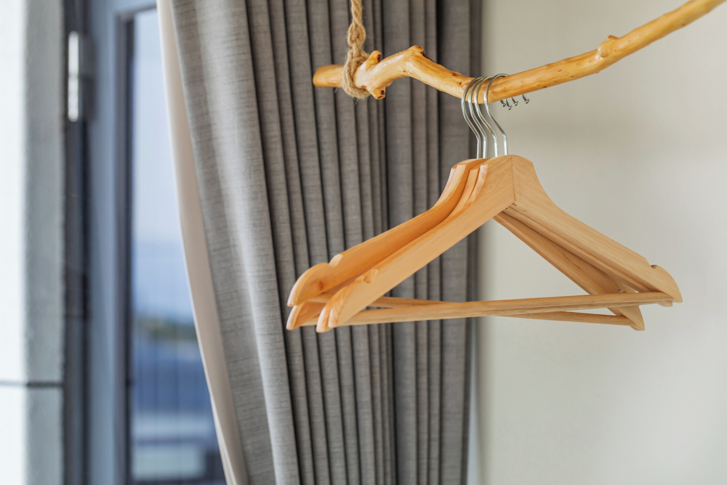 A wooden hanger with a metal hook, hanging against a grey curtain.