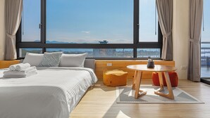 A modern hotel room with a large window, a bed with neatly folded towels, a round wooden table, and a view of the cityscape. - Between River and Sea (Wujie)