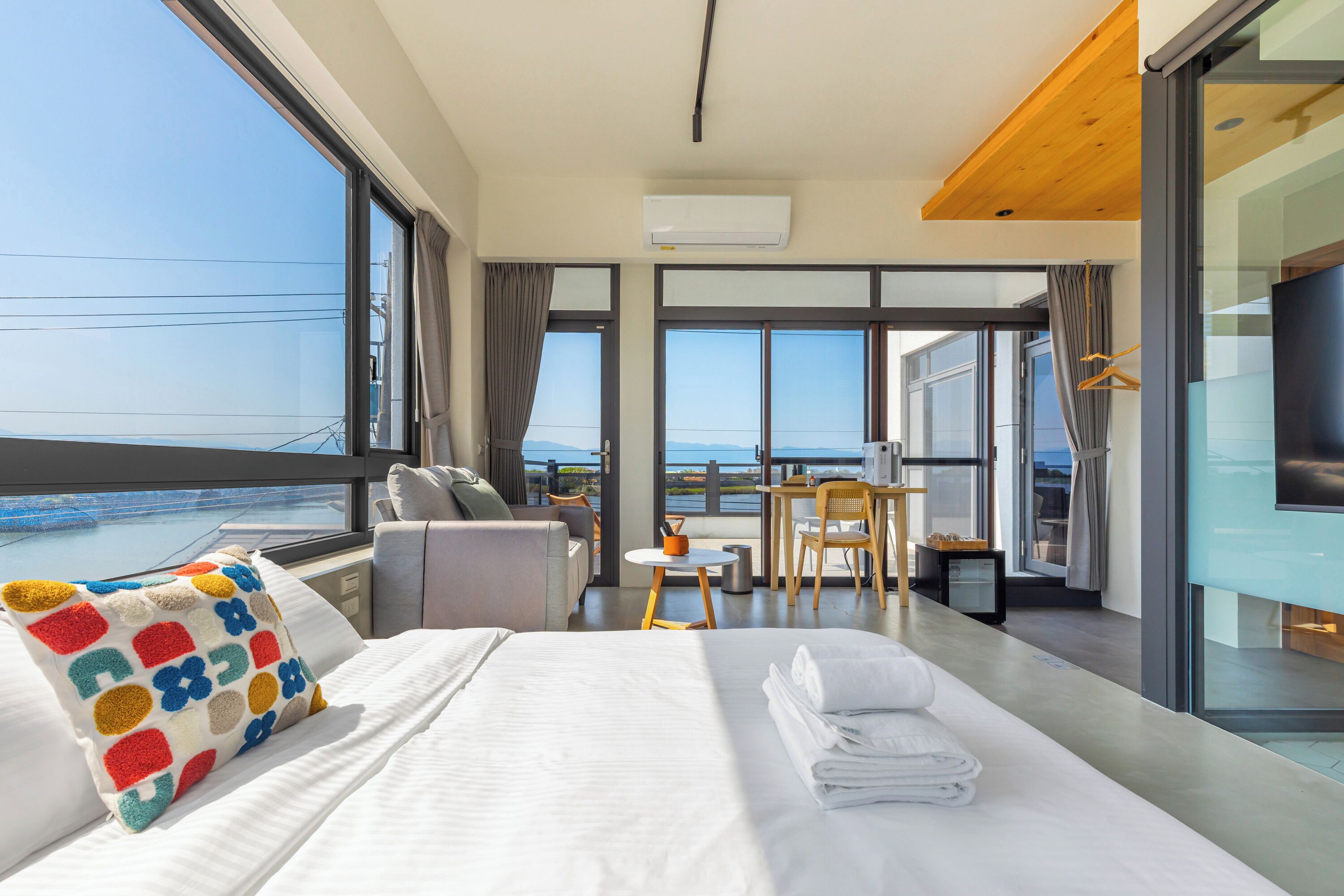 A modern hotel room with a large bed, a desk, and a view of the sea.