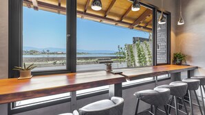 A bar area with a wooden counter, bar stools, and a view of the sea and mountains. - Between River and Sea (Wujie)