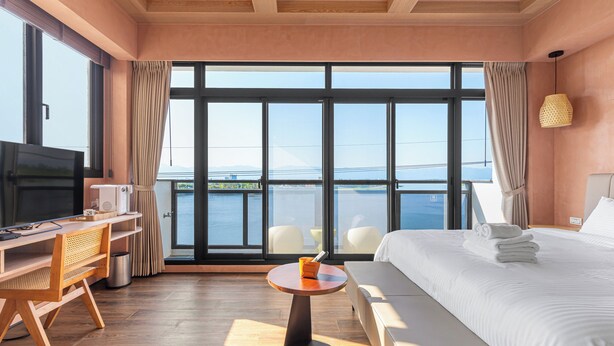A hotel room with a large window, a bed, a desk with a chair, a small table, and a television. - Between River and Sea (Wujie)