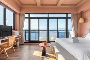 Une chambre d’hôtel avec une grande fenêtre, un lit, un bureau avec une chaise, une petite table et un téléviseur.