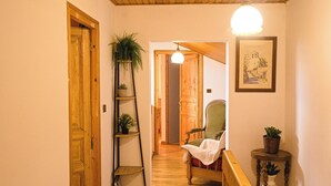 A wooden hallway with a wooden door, a plant on a ladder, a chair, and a small table with a plant. - Cosy mountain home ideal for families and friends. (Angoustrine-Villeneuve-des-Escaldes)