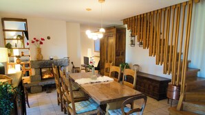 A spacious dining area with a long wooden table, cushioned chairs, and a fireplace. - Cosy mountain home ideal for families and friends. (Angoustrine-Villeneuve-des-Escaldes)