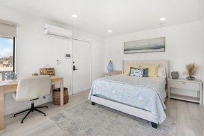 Een slaapkamer met een bed, nachtkastjes, een bureau en een airconditioning.