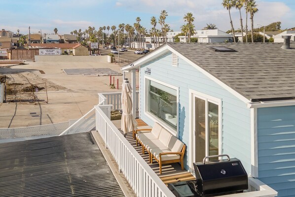 A light blue building with a balcony, a grill, and a view of palm trees and other buildings.