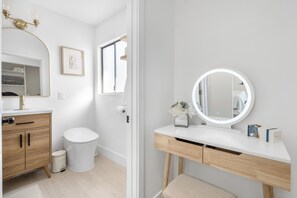 Een moderne badkamer met een wit wastafelmeubel, een ronde spiegel en een toilet.
