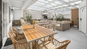 Une terrasse extérieure avec une table en bois et des chaises en osier, un mur en pierre et un espace barbecue intégré.