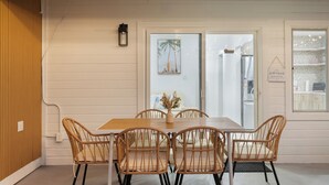Un coin repas avec une table en bois et des chaises en osier, un vase rempli de fleurs et un tableau encadré accroché au mur.