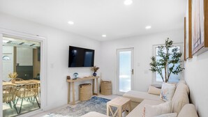 Un salon moderne comprenant un canapé, un téléviseur fixé au mur, un coin repas avec des chaises et une table, ainsi qu’une grande fenêtre offrant une vue dégagée.