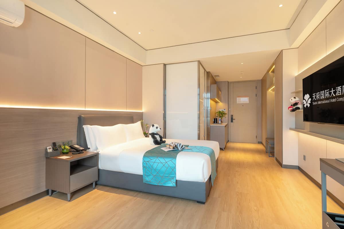 A modern hotel room with a large bed, bedside table, and a TV.