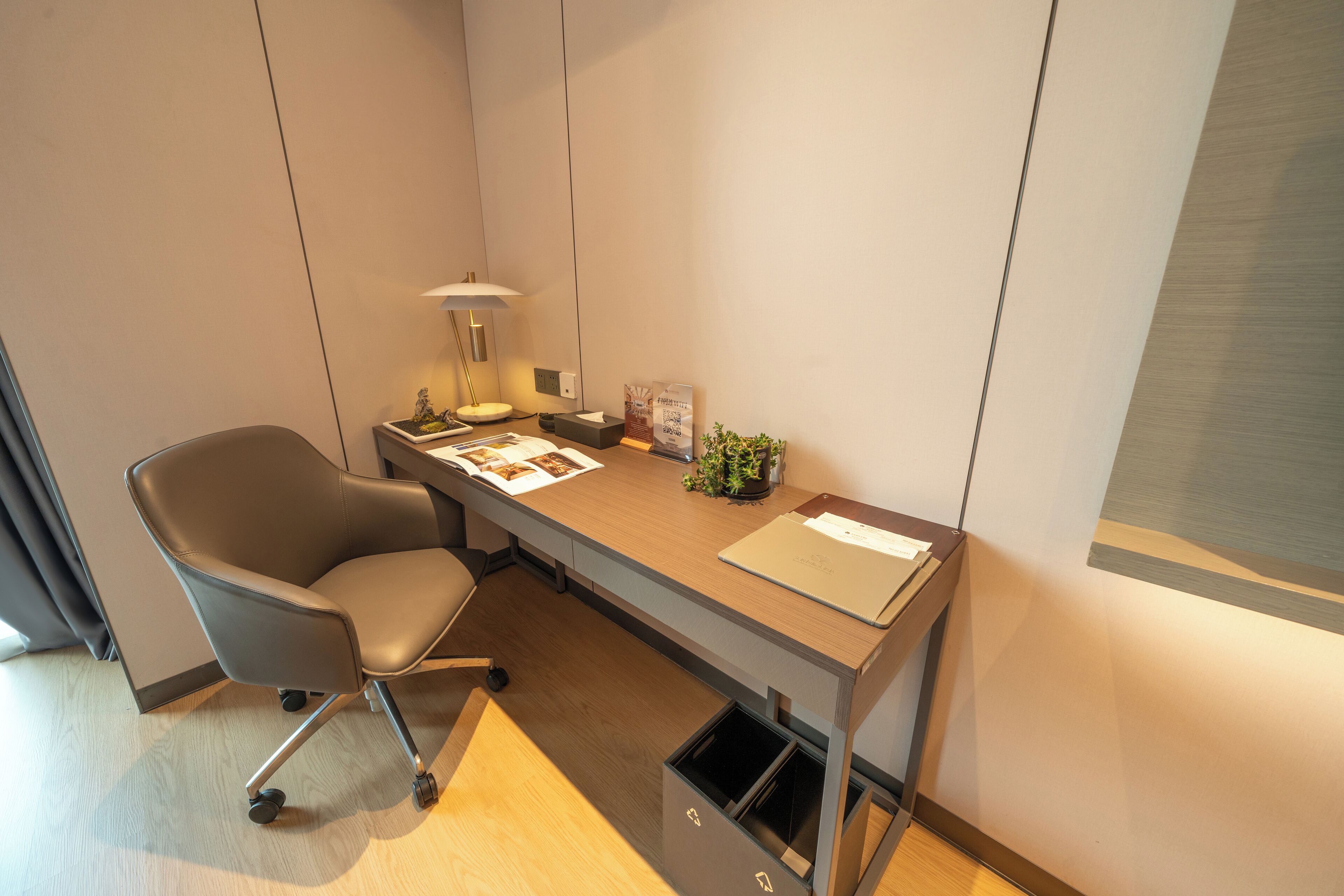 A modern office space with a desk, chair, lamp, and waste bin.