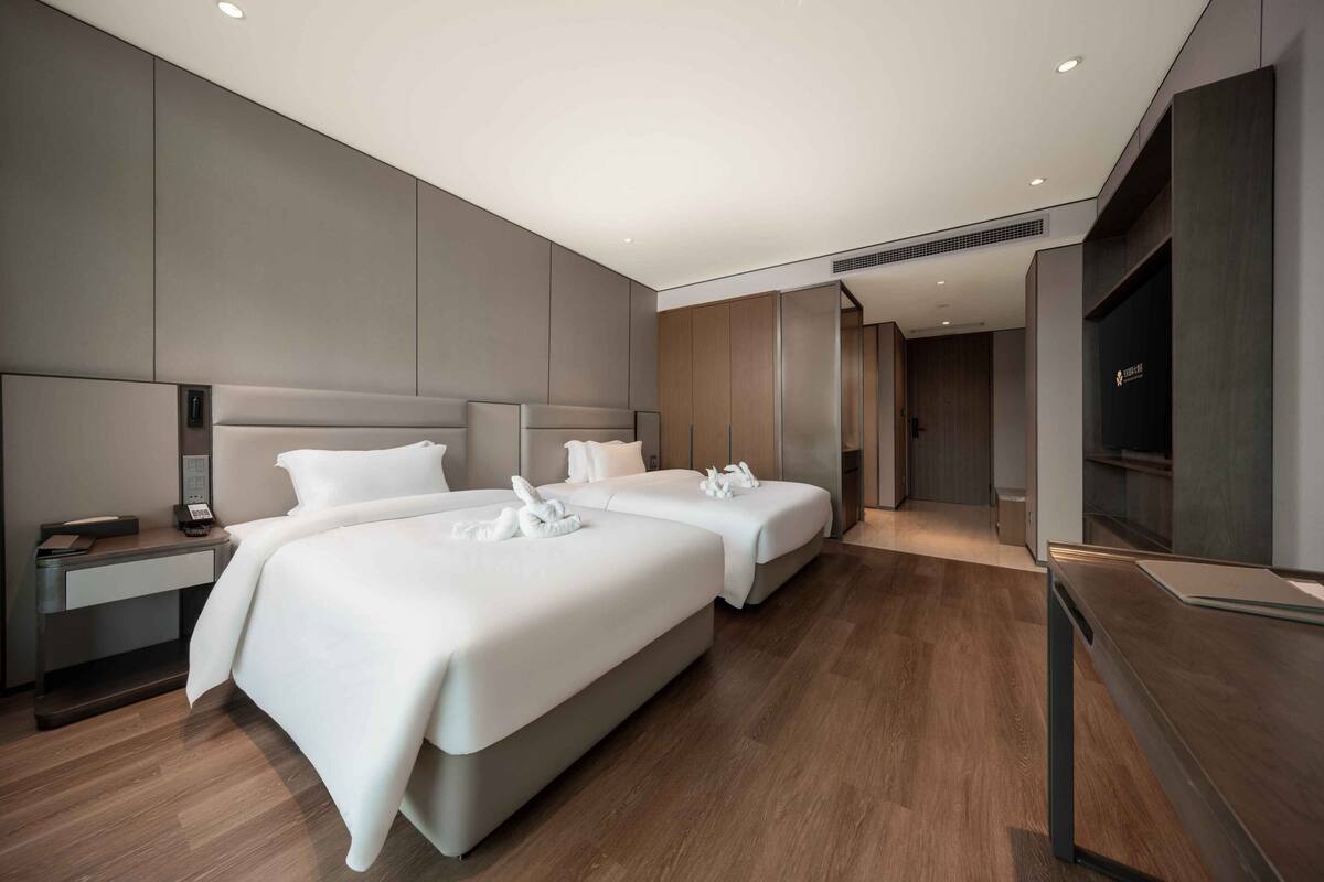 A modern hotel room with two beds, a desk, and a wardrobe.