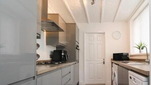 A narrow kitchen with a stove, sink, and dishwasher. - Kitty Cottage - 3 Bedroom - Warm and Welcoming - Sleeps 5 - Blackpool (Blackpool)