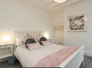 A bedroom with a white bed, two bedside tables with lamps, a grey trash bin, and a framed artwork on the wall. - Kitty Cottage - 3 Bedroom - Warm and Welcoming - Sleeps 5 - Blackpool (Blackpool)