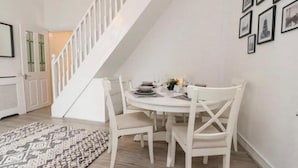 A dining area with a white table and chairs, a patterned rug, and a staircase leading to another room. - Kitty Cottage - 3 Bedroom - Warm and Welcoming - Sleeps 5 - Blackpool (Blackpool)