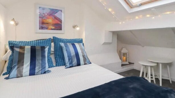 A bedroom with a skylight, a bed with striped pillows, a painting on the wall, and a small table with two chairs. - Kitty Cottage - 3 Bedroom - Warm and Welcoming - Sleeps 5 - Blackpool (Blackpool)