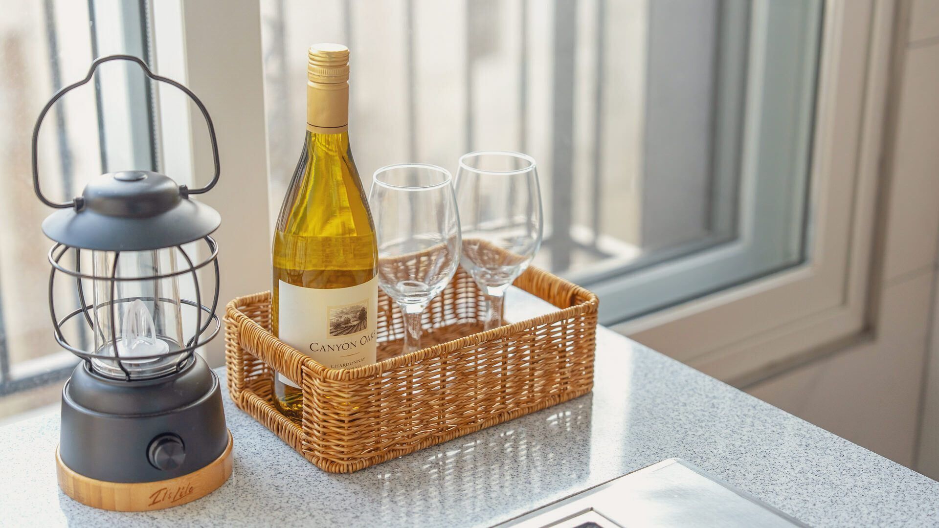 A bottle of Canyon Oak Chardonnay, two glasses, and a lantern on a kitchen counter.