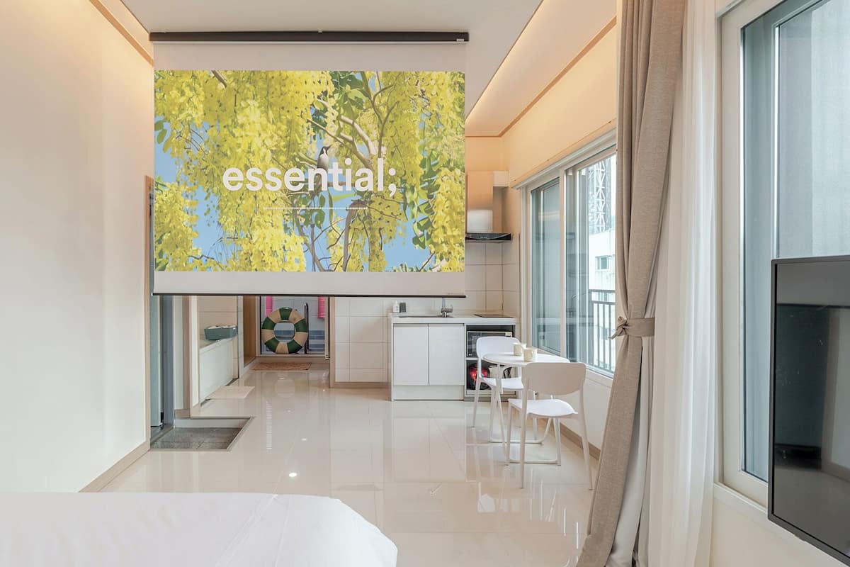 A modern hotel room with a large window, a kitchenette, and a view of a tree.