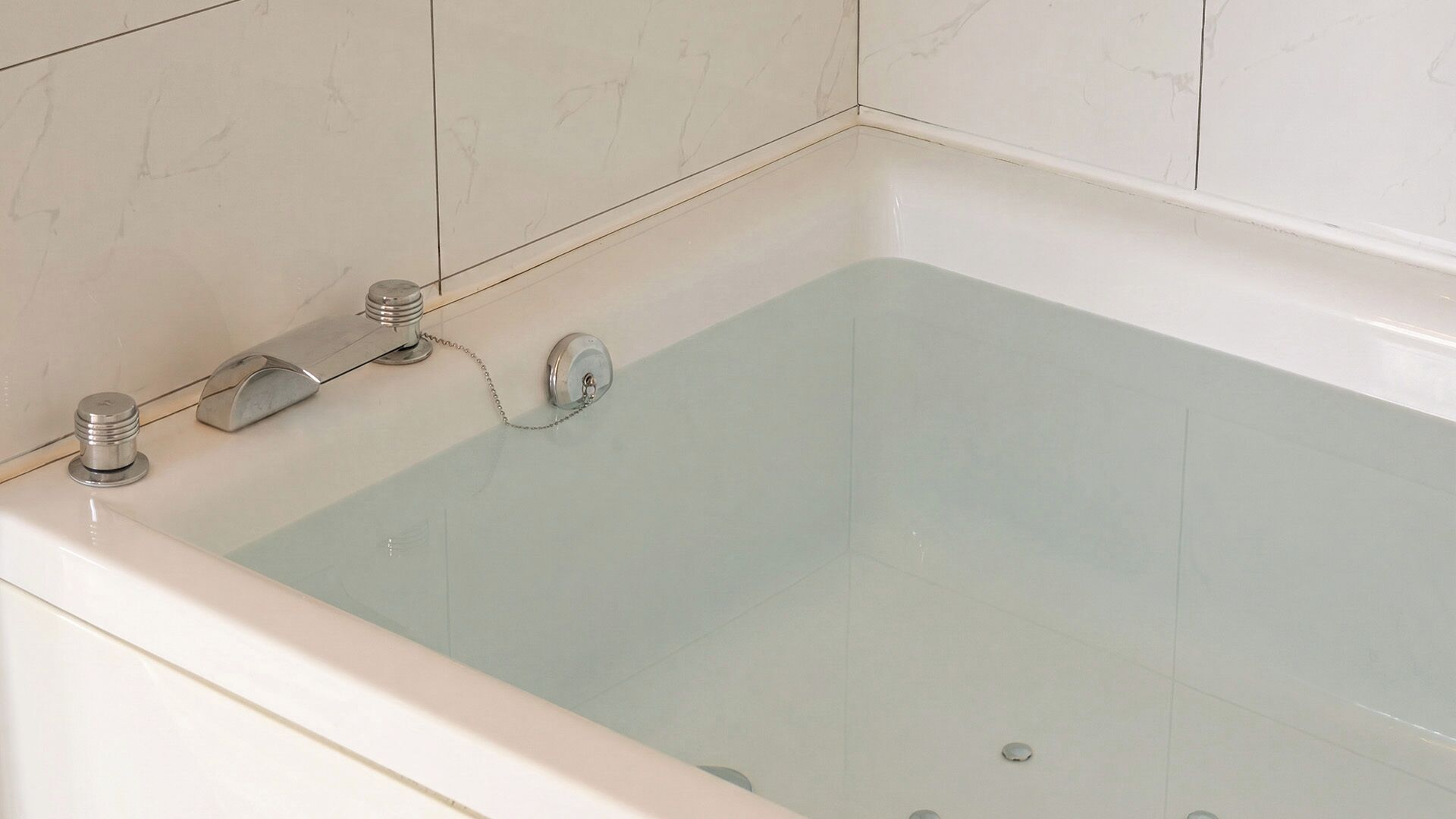 Une baignoire avec un robinet et un bouton de commande, placée devant un mur carrelé.