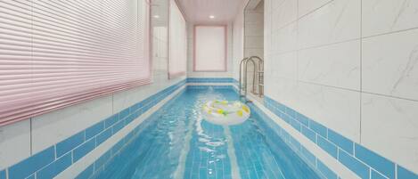 A narrow indoor swimming pool with blue tiles, a floating ring, and a ladder.