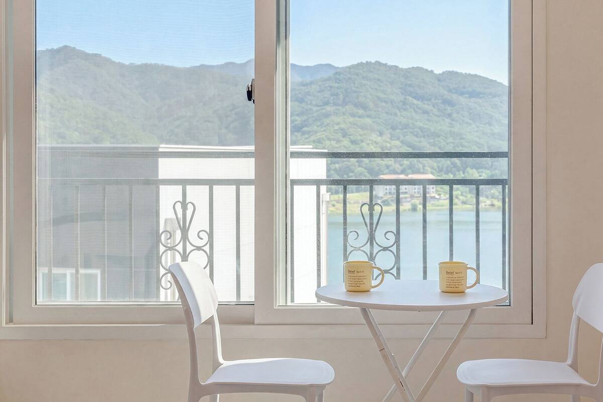 A balcony with a table and chairs, a view of mountains, and a lake.