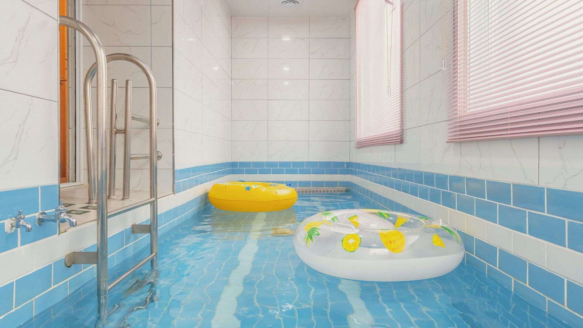 Una piscina con dos flotadores inflables, una zona de ducha con paredes de vidrio y paredes con azulejos azules.