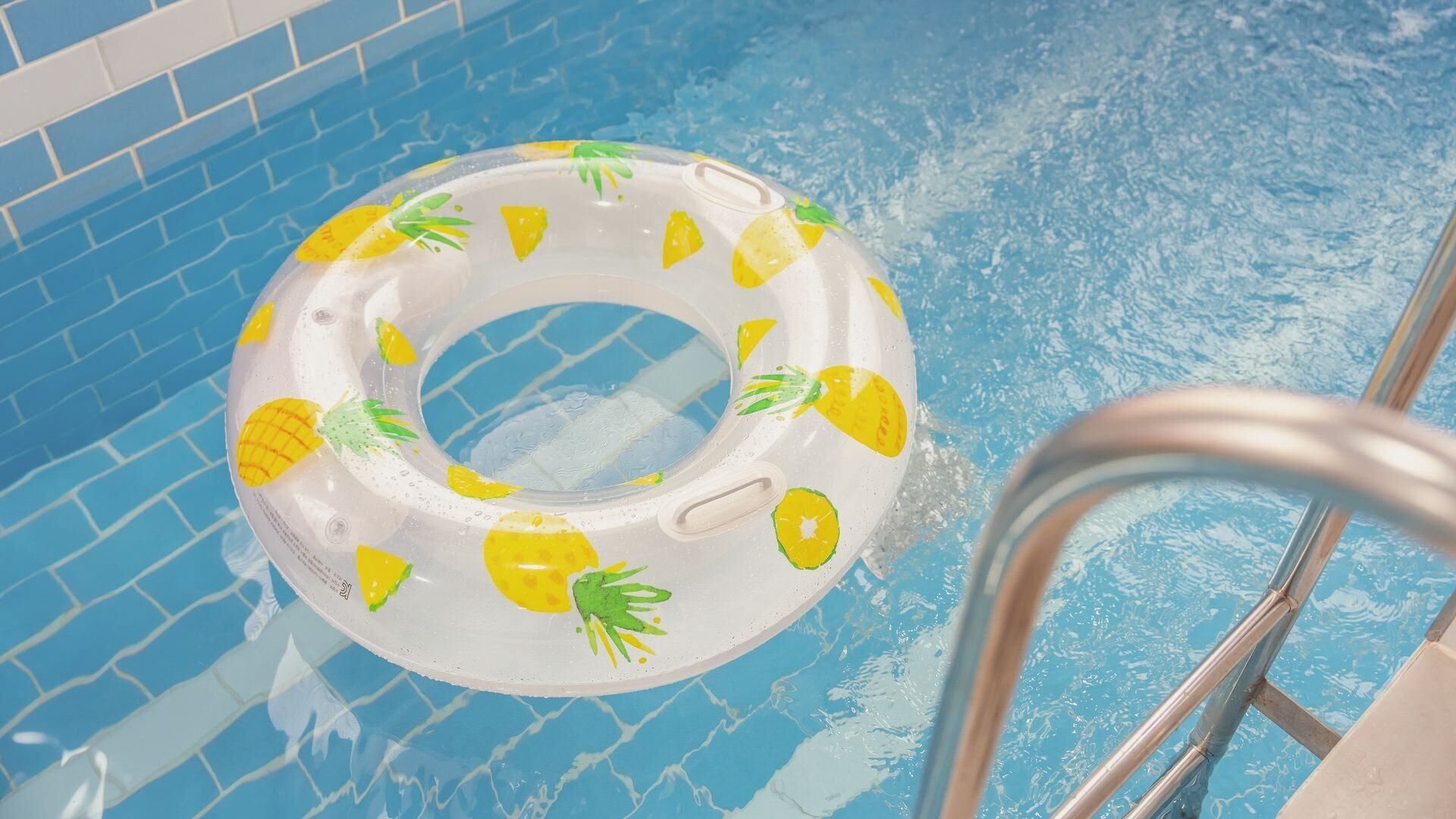A pool with a clear water surface, a metal ladder, and a floating pool ring with a pineapple design.