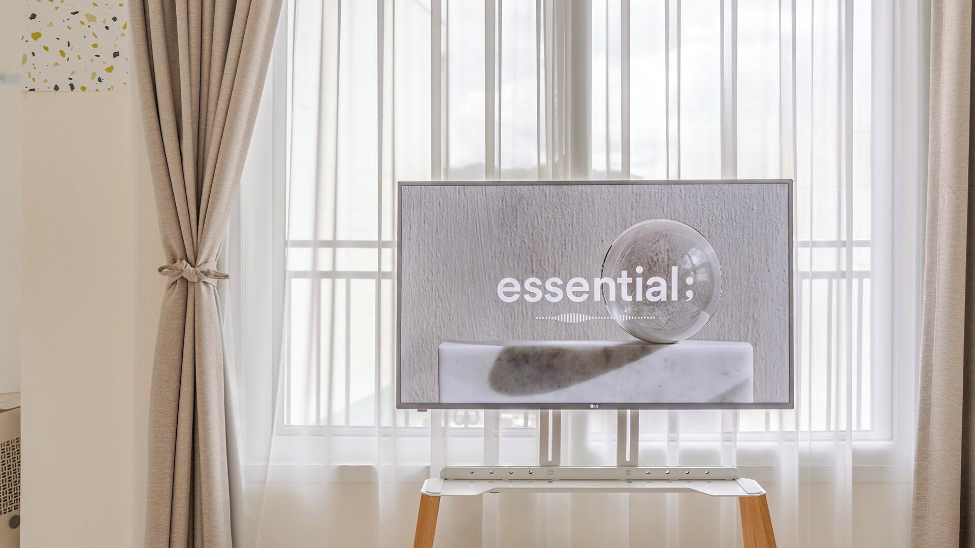 A flat-screen TV on a stand with a marble and a glass sphere, positioned in front of a window with curtains.