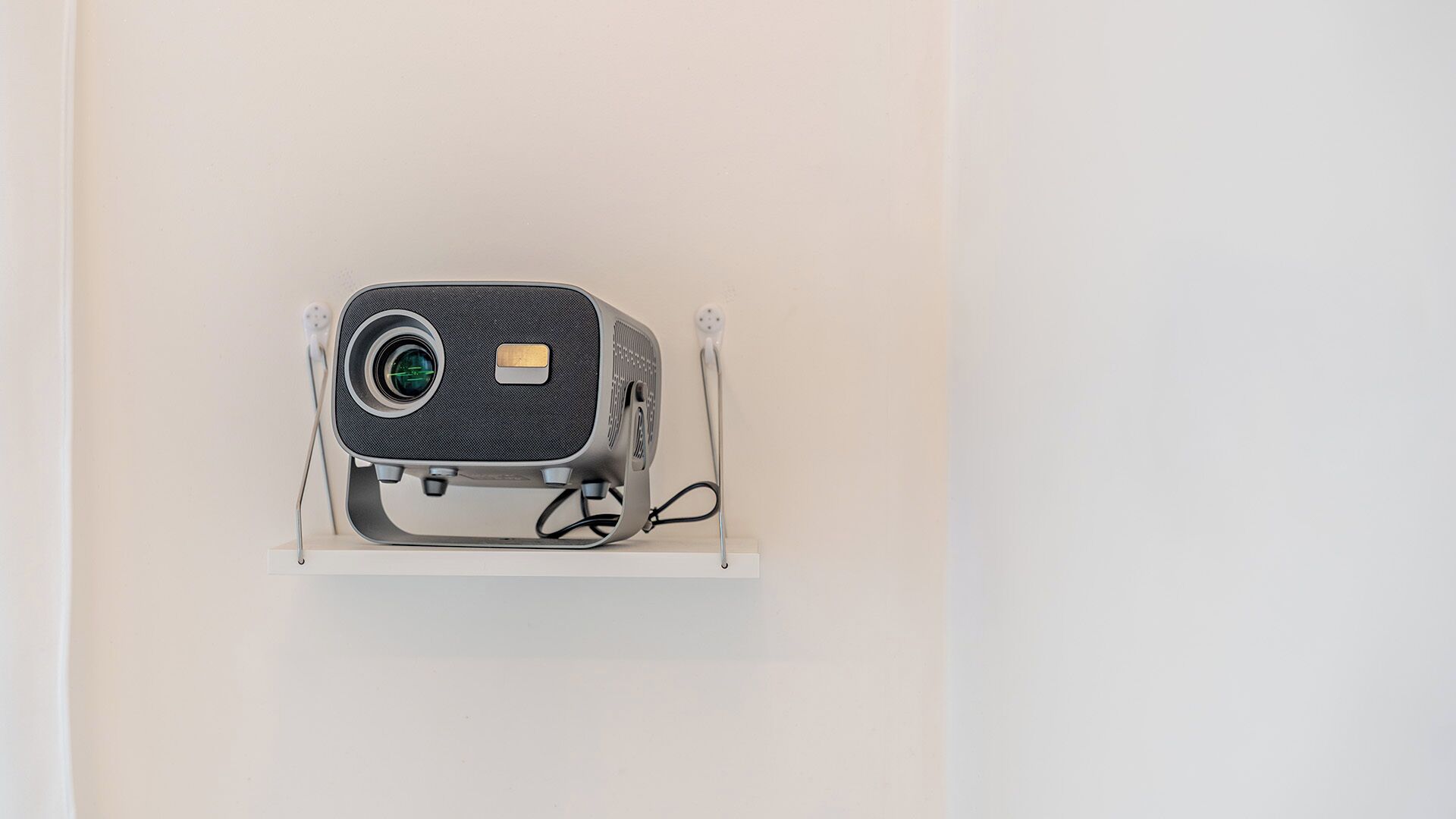 A projector mounted on a white shelf against a plain wall.