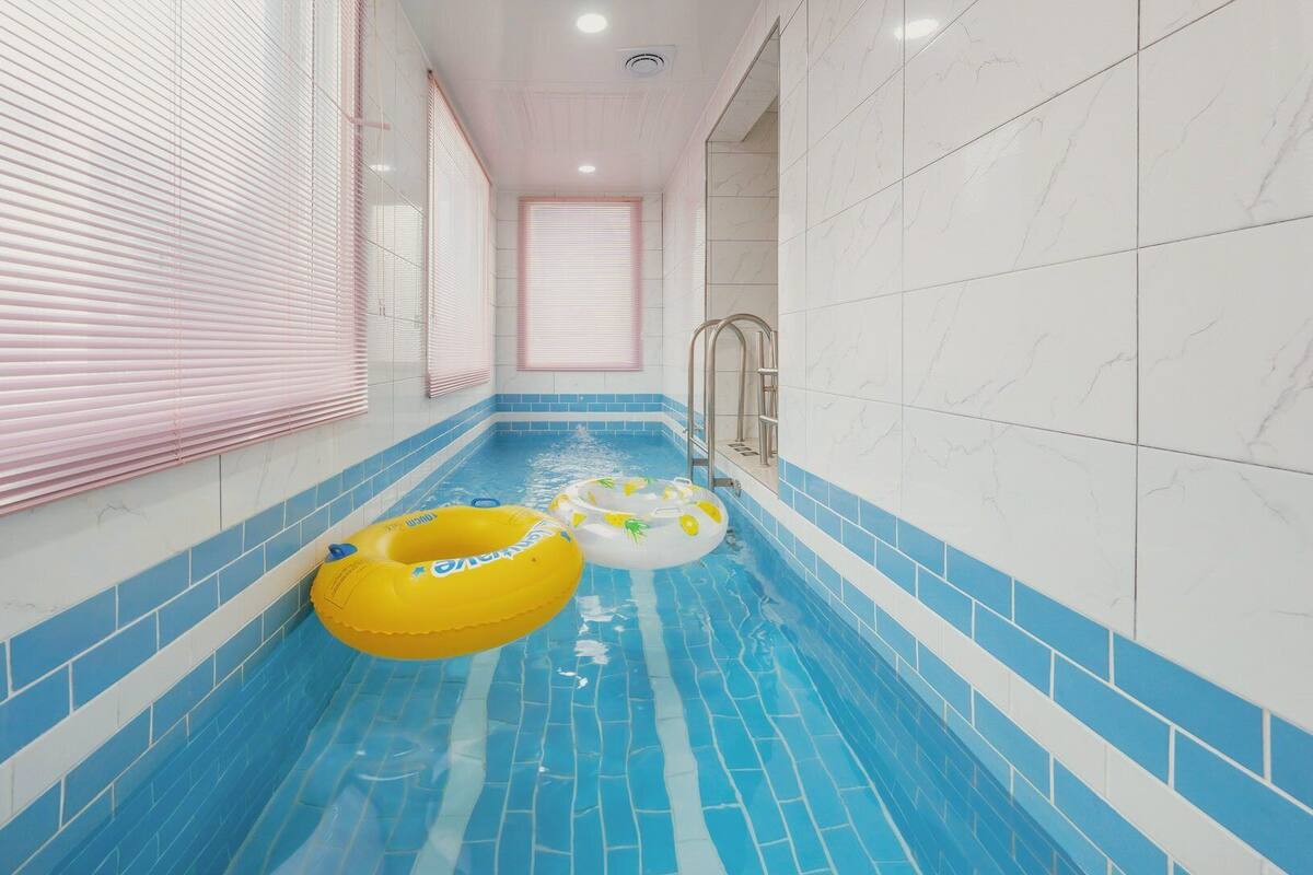 A swimming pool with blue tiles, pink blinds, and two inflatable rings.