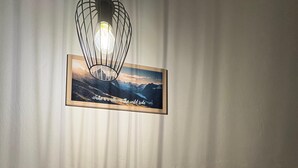 Une pièce avec une table en bois, un tableau encadré au mur, une bouteille de vin, deux verres à vin et une pancarte de bienvenue.