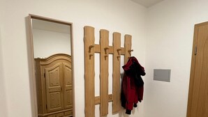 Une pièce avec une armoire en bois, un porte-manteau avec des vestes, et un miroir qui reflète une commode en bois.