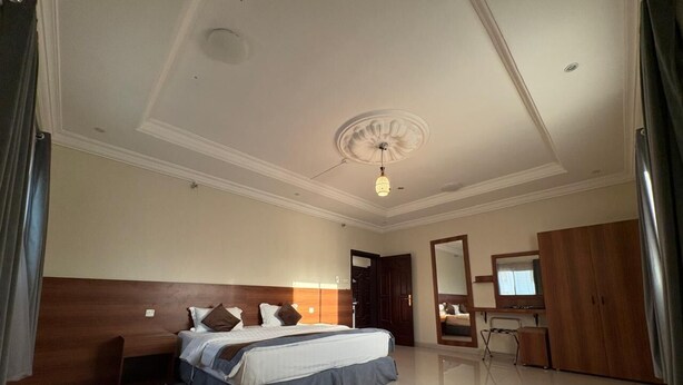 A spacious hotel room with a large bed, a wooden headboard, a desk with a chair, and a mirror. - Lamar Taiba Serviced Apartment (Madinah)