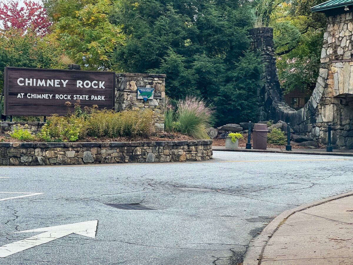 Segnale per il Chimney Rock State Park, con un muro di pietra e aiuole.