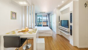 A modern hotel room with a bed, a dining area with a table and chairs, a TV mounted on the wall, and a balcony with a view. - Geoje Kkachi and Santorini Pension (Geoje)