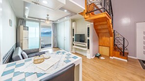 A modern living room with a sofa, a table with a lace tablecloth, a TV, and a wooden staircase. - Geoje Kkachi and Santorini Pension (Geoje)