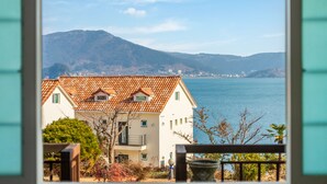 A coastal building with a tiled roof, a balcony, and a view of the sea and mountains. - Geoje Kkachi and Santorini Pension (Geoje)