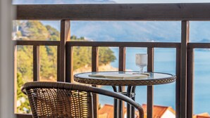 A balcony with a round table, a glass, and a book, overlooking a scenic view of a body of water and mountains. - Geoje Kkachi and Santorini Pension (Geoje)
