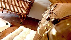 A room with a wooden crib, a patterned sofa, and a glass bottle with a cork. - Il suono del fiume (Bagnone)