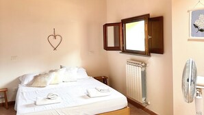 A bedroom with a wooden bed, a radiator, a mirror, and a wall-mounted fan. - Il suono del fiume (Bagnone)