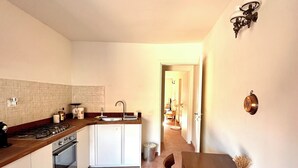 A compact kitchen with a stove, sink, and cabinets, leading to a dining area with a table and chairs. - Il suono del fiume (Bagnone)