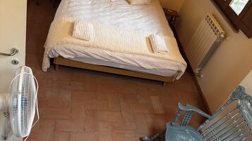 Une chambre à coucher avec un lit, un radiateur, un fauteuil à bascule et un ventilateur.