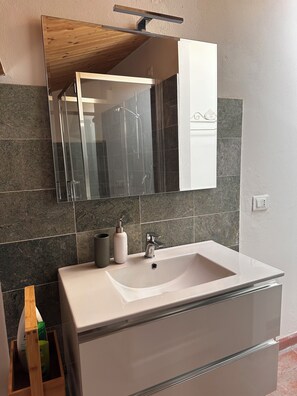 A bathroom with a large mirror, a sink, and a wooden cabinet. - Il suono del fiume (Bagnone)