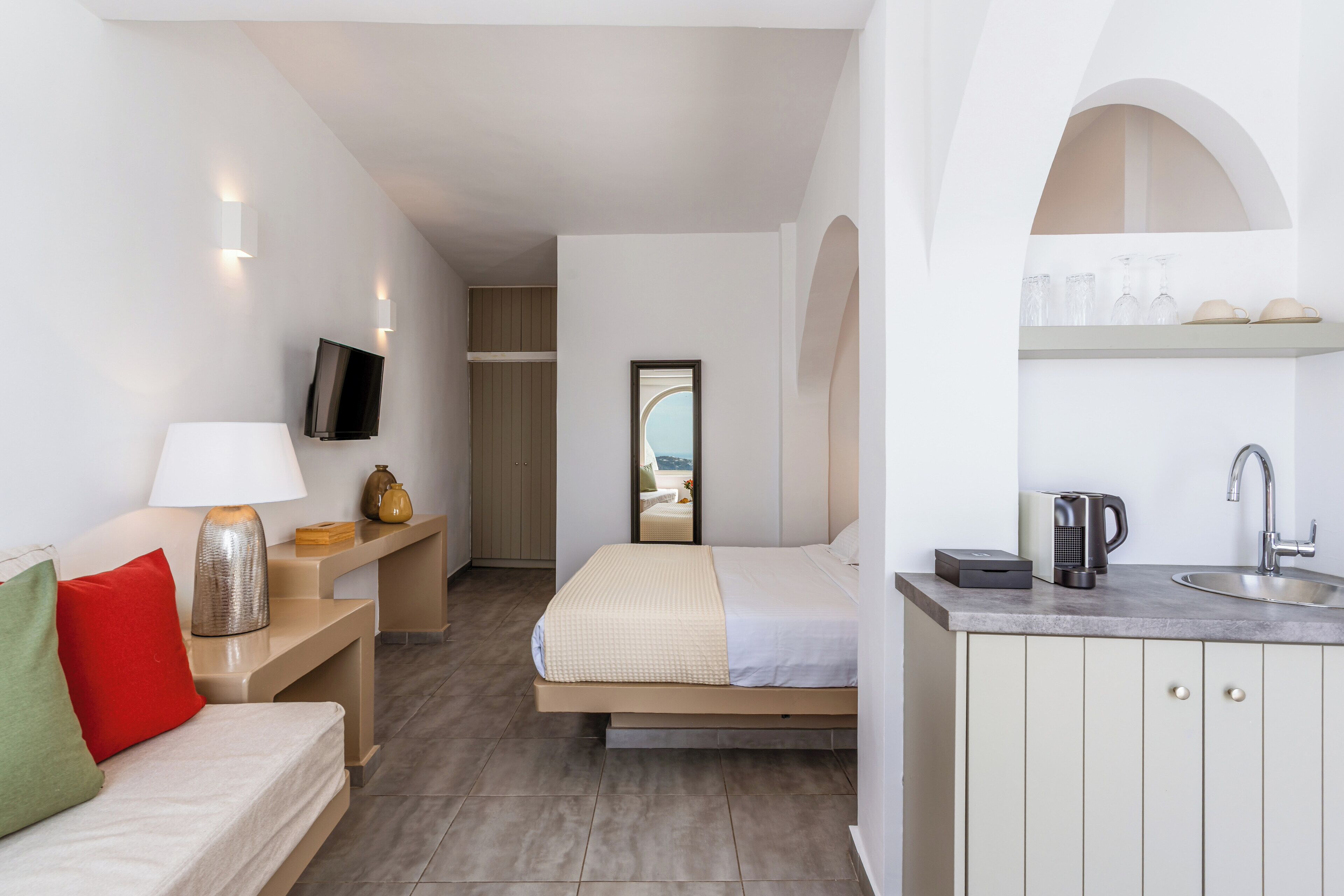 Habitación de hotel moderna con cama, mesita de noche, lámpara y vista al mar a través de una ventana.