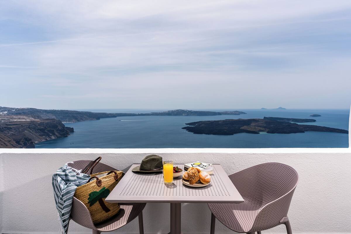 Una mesa con vista al mar, un sombrero, un bolso de paja y un plato con comida y una bebida.