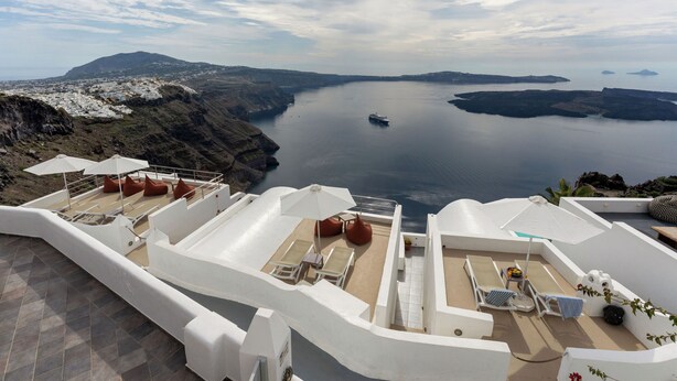 Une terrasse sur le toit, dotée de chaises longues blanches, d’un parasol et offrant une vue sur une mer calme et des îles lointaines.