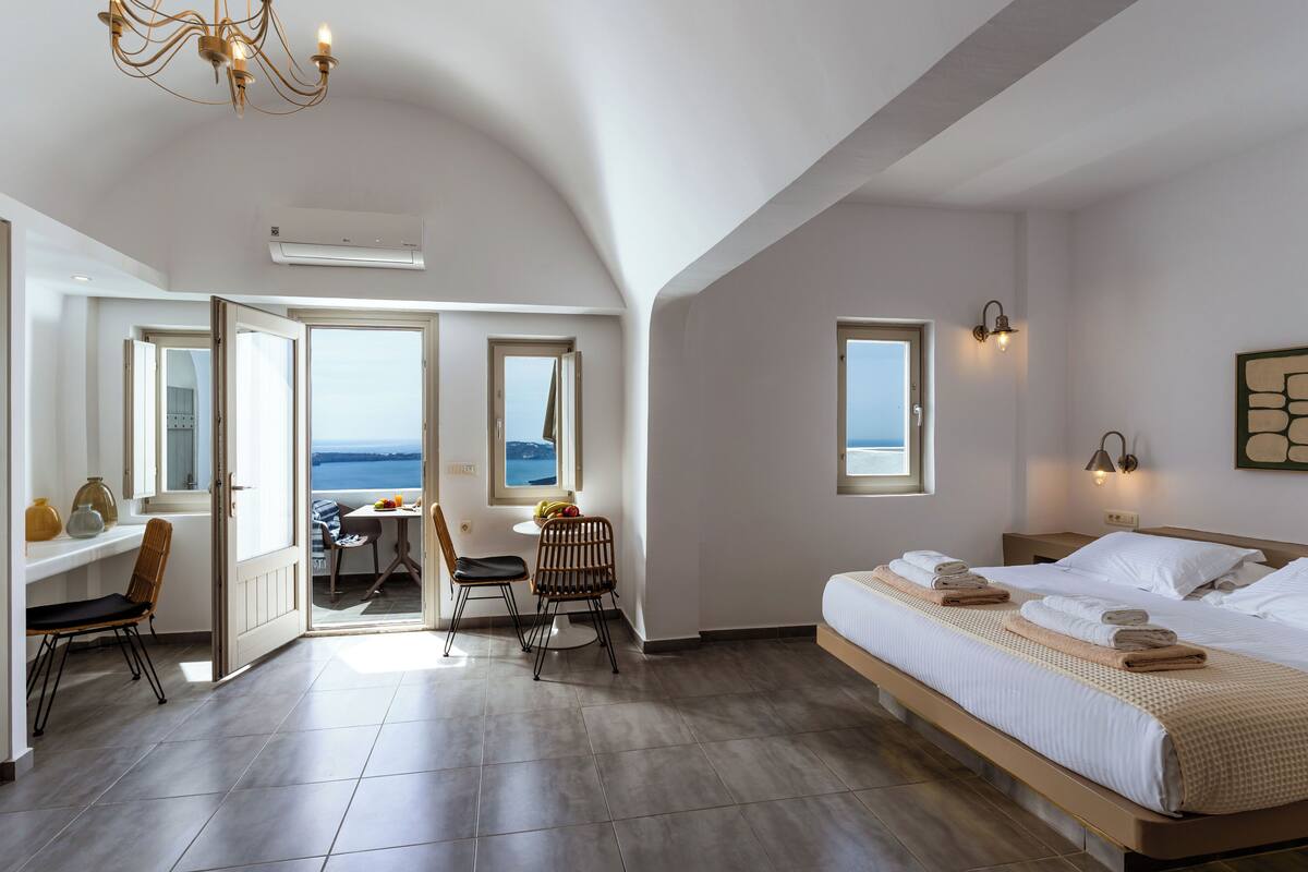 Una habitación de hotel moderna con una cama grande, un área de comedor y vista al mar.